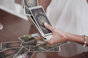 L'art de la cartomancie illustré : des cartes d'un oracle étalées sur une table, avec des motifs complexes représentant des symboles comme des figures, des pièces et des baguettes, tandis qu'une main tient un paquet de cartes prêt à révéler des réponses